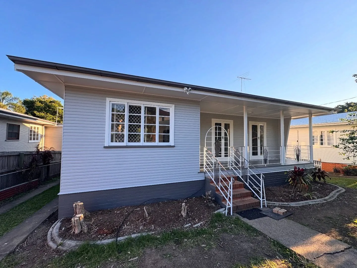 Front of a light grey weatherboard house in Annerley with white window frames, white stair railings and a dark base