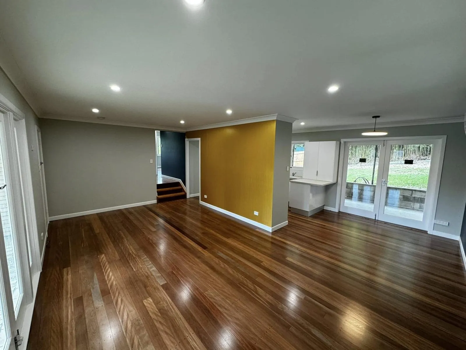 Living area with light grey walls, a gold feature wall, white trims and polished timber floors