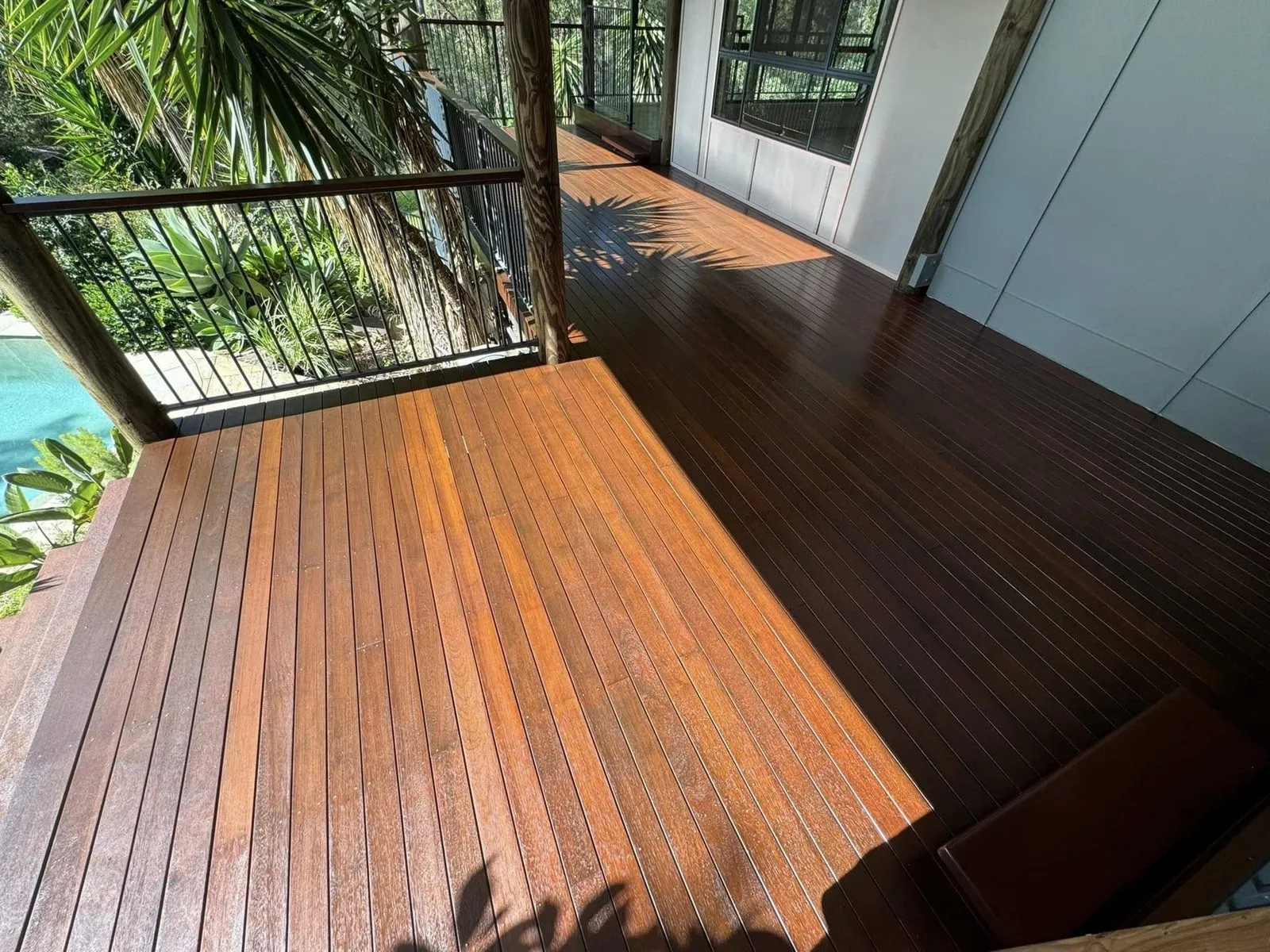 Corner of an oiled hardwood deck with black railings and tropical plants beyond