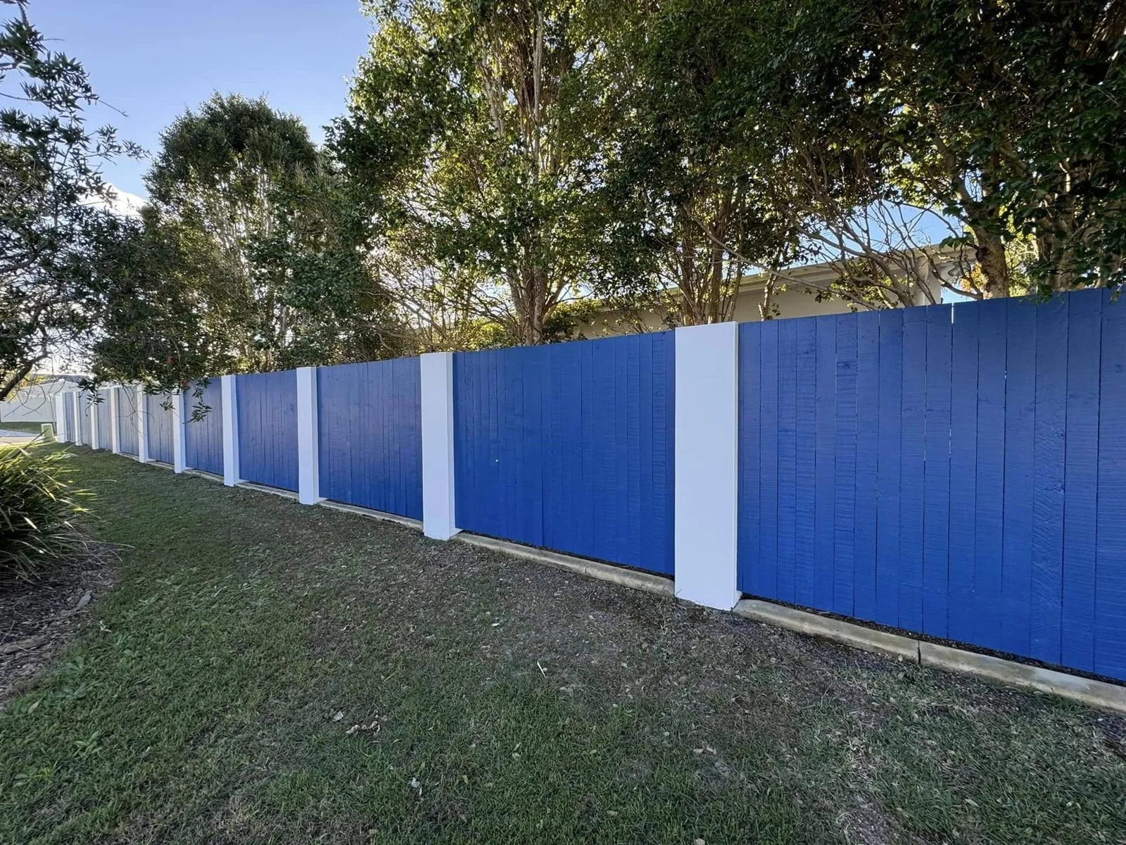 Blue fence panels between white rendered piers along a lawn